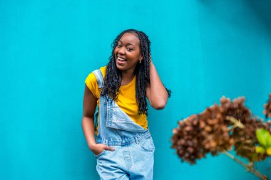 Kopya alanı olan yatay portre ve mavi bir şehir duvarına yaslanmış utangaç pozlar veren sıradan bir Afrikalı kadına odaklan.