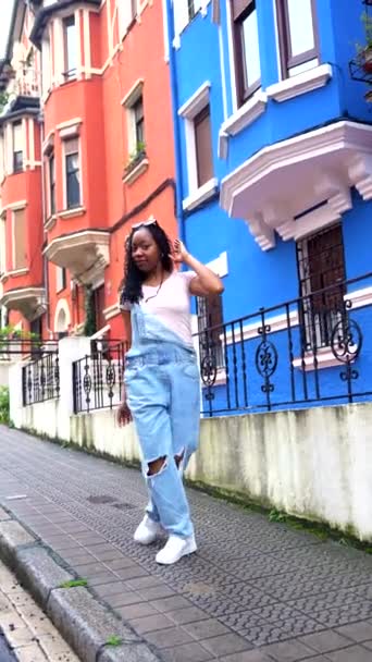 Африканская Женщина Поет Слушая Музыку Наушниках Стоящих Улице Голубыми Домами — стоковое видео
