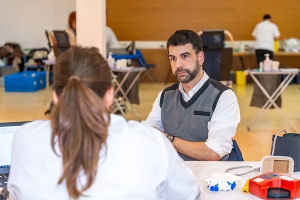 Adult caucasian serious man and nurse talking in a blood donation campaign center with other people around