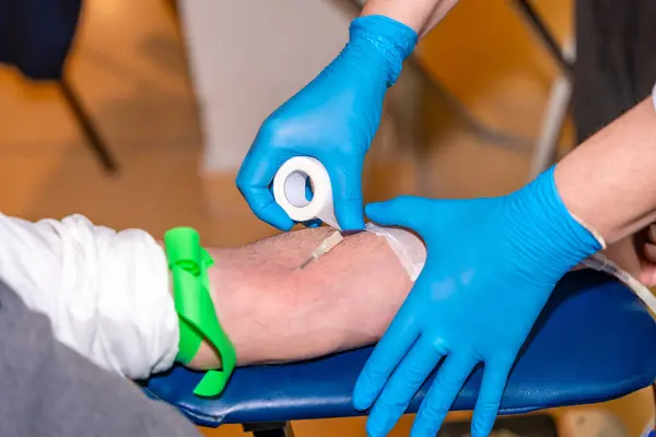 Close-up of a nurse fixing a needle with stripe into the arm of a blood donor