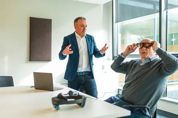 Businessman presenting a innovative mixed reality goggles to a client sitting in the office