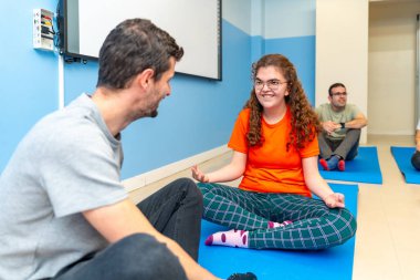 Yoga eğitmeni ve engelli kadın başkalarıyla yoga yaparken konuşuyor.