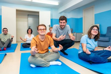 Dost canlısı erkek yoga eğitmeni özel ihtiyaçları ve düşük sendromu olan insanlarla dolu bir sınıfı yönetiyor.