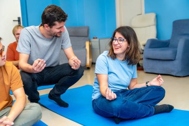 Yoga hocası yoga sınıfında minderde oturan engelli bir kadına nilüfer pozisyonunu öğretiyor.