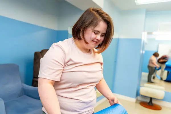Woman with down syndrome pick up a yoga mat after exercising in a gym