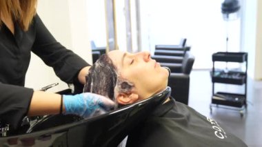 Gözleri kapalı, güzel bir kuaförde saçını yıkayan rahat bir kadın.