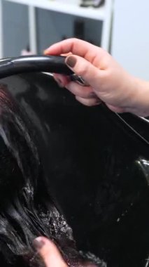 Bir kuaförün elleri, bir kuaförde müşterinin uzun saçlarını yıkıyor.
