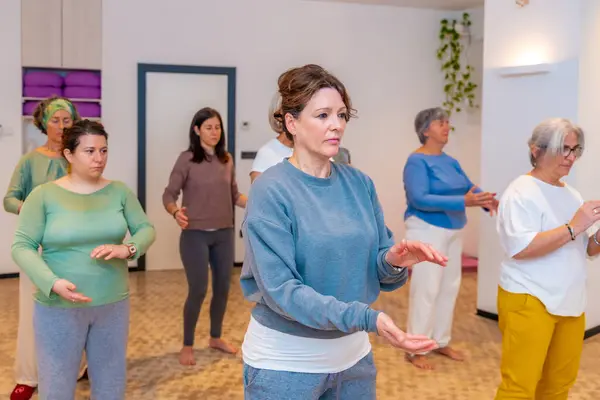 Side view three quarter length photo of a group of a mature adult women moving coordinated join hands in a qi gong class