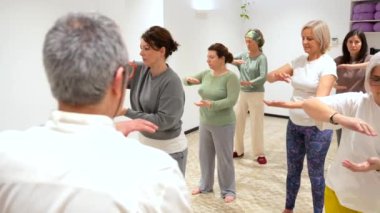 Qi gong erkek, olgun bir öğretmen. Bir sınıf dolusu olgun kadını kapalı bir merkezde yönetiyor.