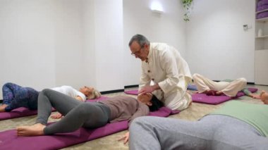 Qi Gong sınıfında nefes alma egzersizi yapan eğitmen yerde yatan birkaç kadınla birlikte.