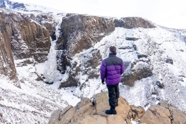 İzlanda 'da kışın donmuş Hengifoss şelalesine bakan maceraperest genç bir adam.