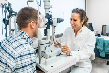 Kadın optometrist klinikte gözlerini kontrol ederken bir hastayla konuşuyor.