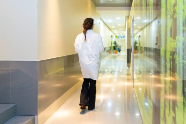 Rear view of a female ophthalmologist walking along a corridor in the clinic clipart