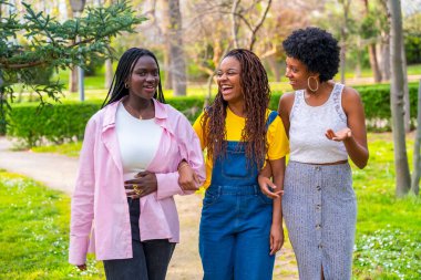 Mutlu Afrikalı genç bayan arkadaşlar park yolunda kol kola yürüyorlar.