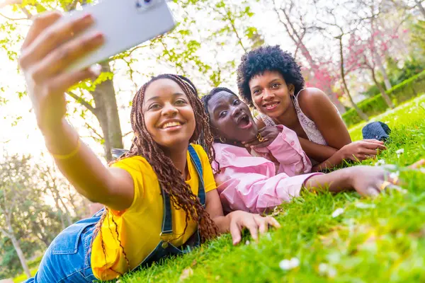 Üç Afrikalı bayan arkadaş şehir parkında selfie çekiyorlar.