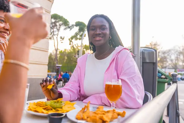Hymyilevä Afrikkalainen Nuori Nainen Syö Nachoja Ystävien Kanssa Ulkona Ravintolassa kuvapankin valokuva