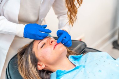 Kozmetik uzmanı, klinikte beyaz yetişkin bir kadının yüzüne botoks yapıyor.