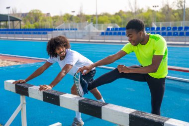 İki genç Afro-Amerikan sporcusu koşu pistinde bacaklarını açarken dikkatleri dağılıyor.