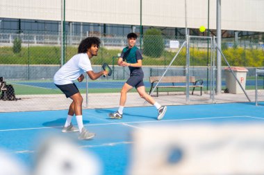 Çok ırklı genç sporcu arkadaşlar güneşli bir günde açık havada penisbol oynuyorlar.