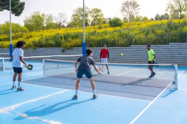 Açık hava sahasında Pickleball oynayan dört farklı etnik gruptan oluşan bir grubun tam boy fotoğrafı.