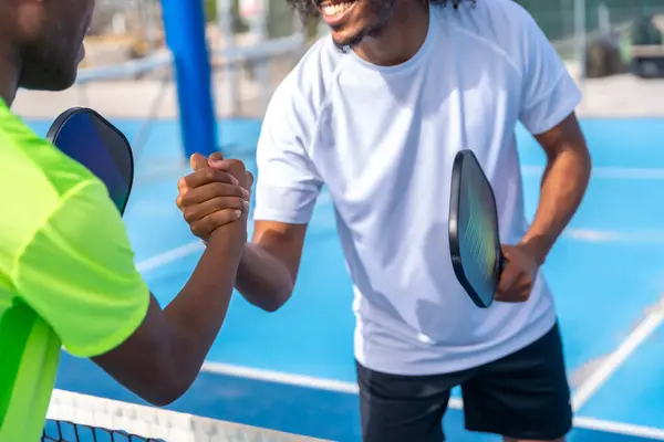 Pickleball Afro-Amerikan erkek rakipleri açık hava sahasında maç yapmadan önce el sıkışıyor.