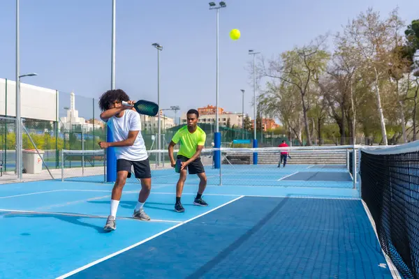 İki Afrikalı sporcu arkadaşın açık havada birlikte tenis oynamalarının fotokopi çekilen tam boy fotoğrafı.