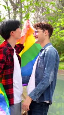 Çoklu etnik çeşitliliği kutlayan eşcinsel bir çiftin düşük açılı görüntüsü bir parkta lgbt bayrağı sallıyor