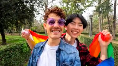 Igbt bayrağını sallayan çok ırklı eşcinsel çift şehir parkında çeşitliliği kutluyor.