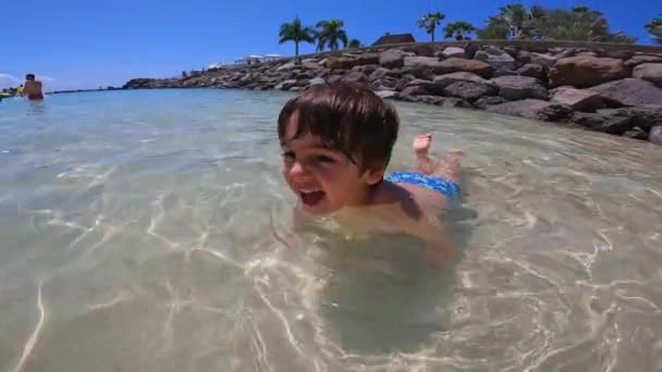 少年が海で泳いでいる 水は澄み切って穏やかである 少年は青い水着を着ている 動画クリップ