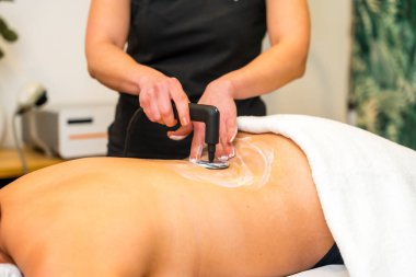 Tanımlanamayan bir fizyoterapistin INDIBA elektrikli aletini kullanarak bir hastanın sırtına baskı uygulayarak yakın plan görüntüsü.