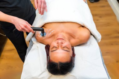 Bir klinikte sedye üzerinde yatan bir hastanın omuz ağrısını hafifletmek için INDIBA makinesini kullanan masaj terapisti.