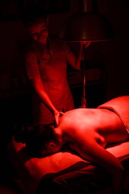 Kırmızı ışık kullanan bir kadın fizyoterapi merkezinde sıcak masaj yaptırıyor.