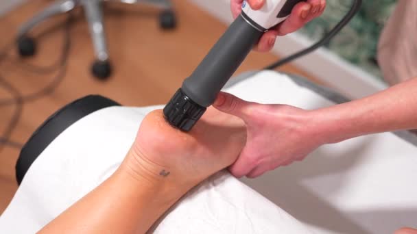 ホリスティッククリニックで足に衝撃波療法マッサージを受けるストレッチャーの認識できない患者のクローズアップ — ストック動画
