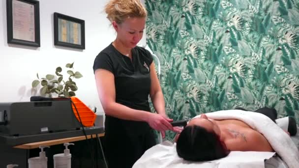 인디바 도구를 사용하여 클리닉에서 스트레치에 누워있는 환자의 어깨에 통증을 치료하는 — 비디오