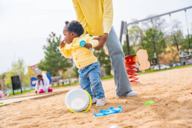 Tanımlanamayan Afrikalı bir annenin düşük açılı fotoğrafı parktaki sevimli Afrikalı bir kızın yanına yürümesine yardımcı oluyor.