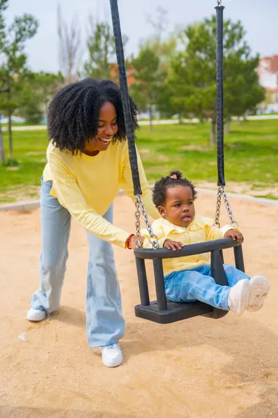 公園で幸せなアフリカの女の子と母親の垂直写真 スイングと笑顔 — ストック写真