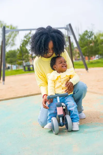 公園で自転車に乗る少女を助ける幸せなアフリカの母親の垂直写真 — ストック写真
