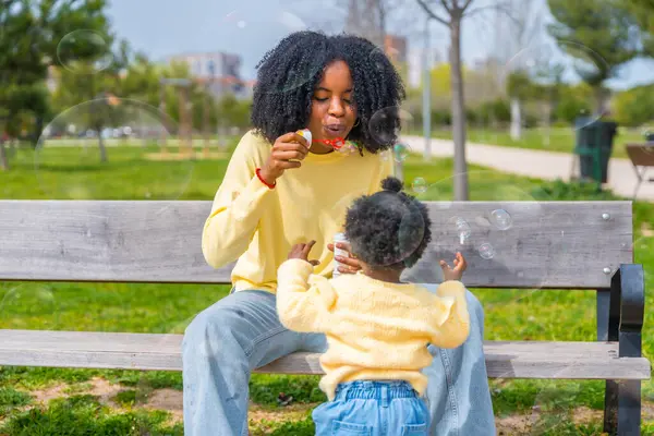 一个非洲妇女和女儿在公园玩肥皂泡的正面四分之三长的照片 — 图库照片