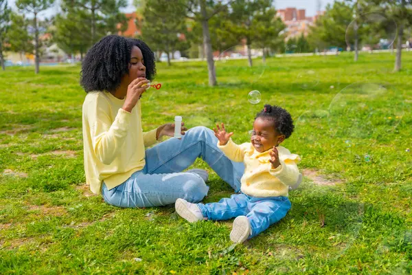 公園のアフリカの母と少女は晴れた日に石鹸の泡を作る芝生 — ストック写真