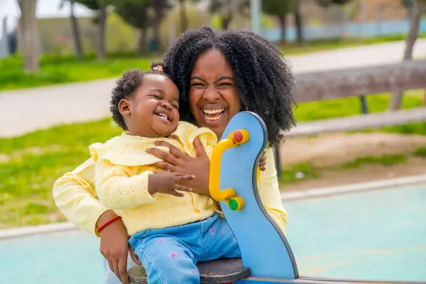 Felice Madre Africana Che Ride Abbracciando Sua Figlia Seduta Altalena Foto Stock