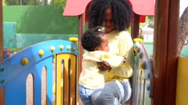 Genç bir Afrikalı anne ve bebeğin oyun parkında oynaması ön planda.