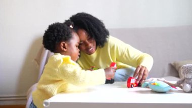 Afrikalı genç güzel anne ve kız evde oyuncak araba oynuyorlar.