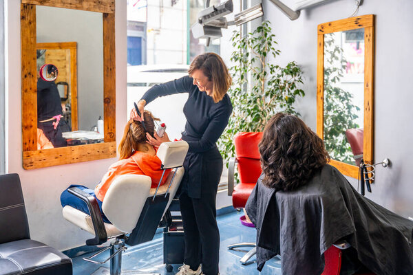 Full length photo of a smiling female hairdresser talking with woman while combing a client in a hair salon
