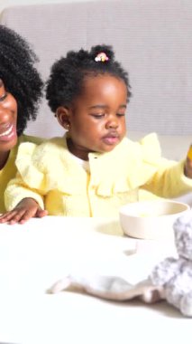 Küçük tatlı Afrikalı kız ve anne kanepede oyuncaklar ve kitaplarla oynuyorlar.