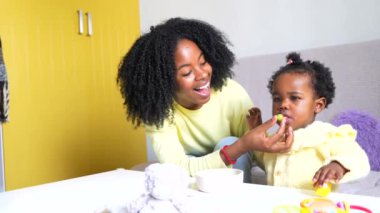 Küçük Afrikalı kız annesinin yanında yemek yemeyi öğreniyor.