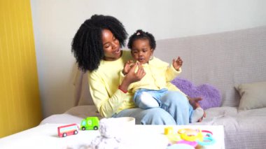 Afrikalı çocuk evde gülümseyen annesinin yanında oturma odasında yemek yiyor.