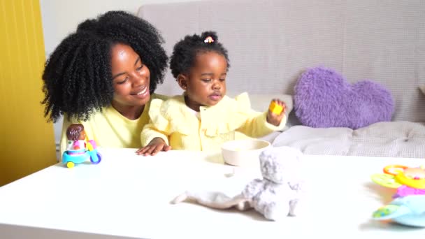 小さなかわいいアフリカの娘とおもちゃや本でソファーで遊んでいる母親 — ストック動画