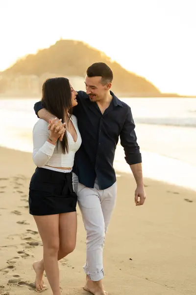 一对年轻貌美的浪漫夫妇在沙滩上欣赏日落的纵向照片 图库图片