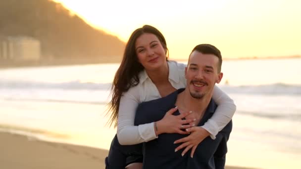 日落时分在海滩上亲吻和骑背的一对情侣的水平照片 图库视频