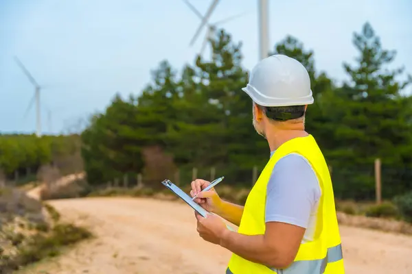 Stock image Rear view of a male mature engineer writing notes inspecting wind turbines in a green energy park